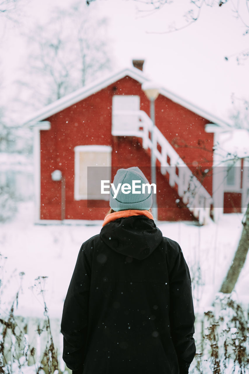 Back view of unrecognizable female in warm outerwear standing in village in winter and enjoying nature