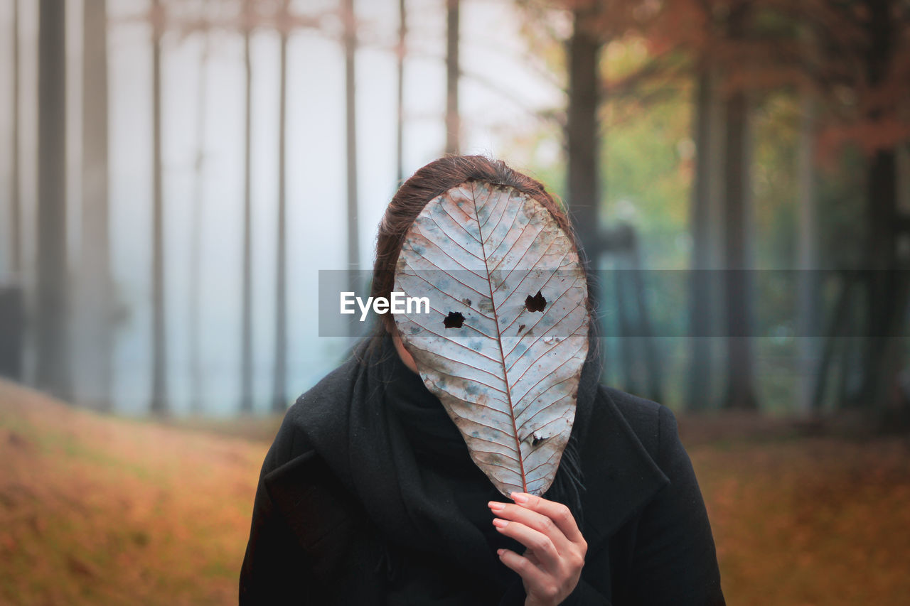 Portrait of person holding autumn leaf outdoors