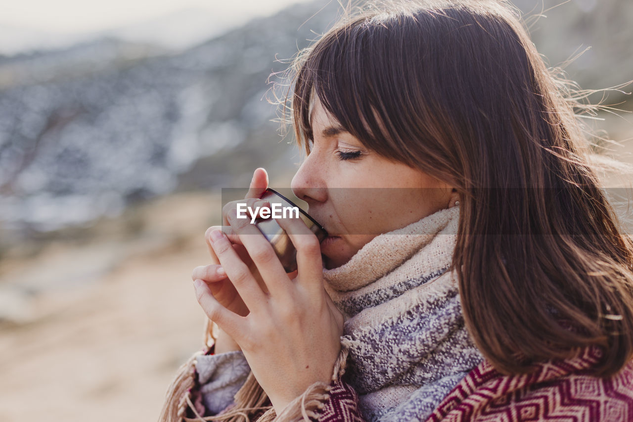 Close-up of woman drinking coffee in container during winter