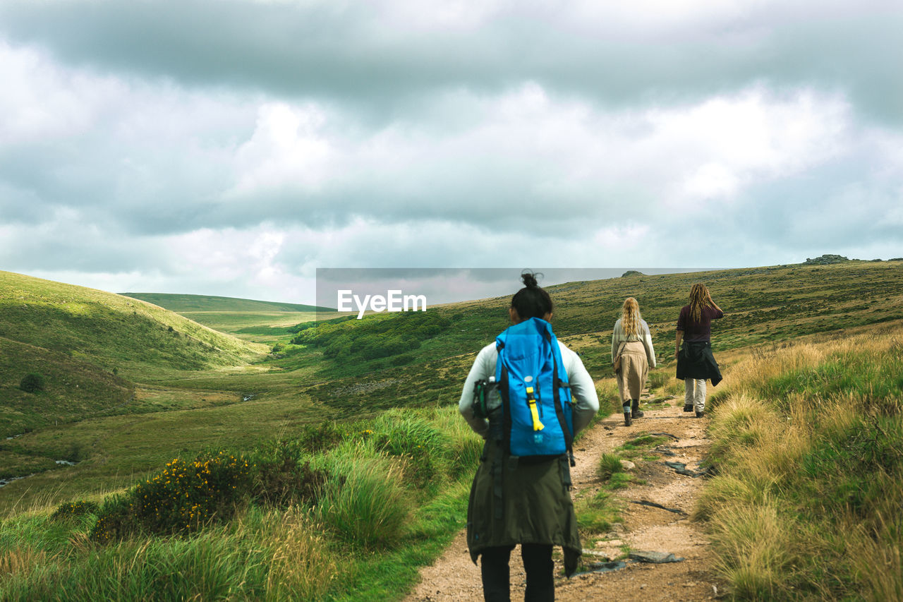 REAR VIEW OF HIKERS WALKING ON MOUNTAIN AGAINST SKY