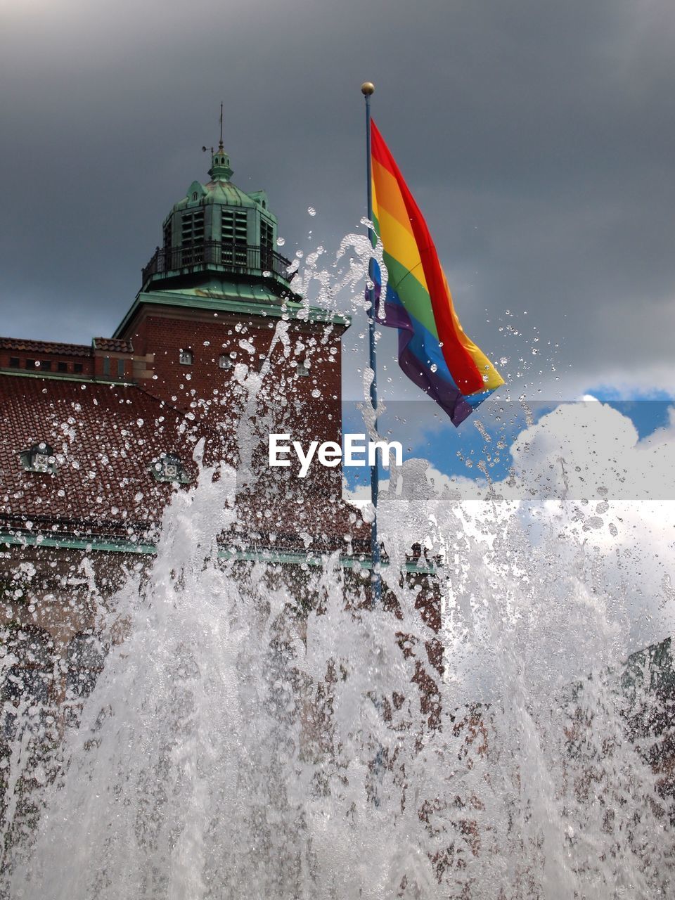 Rainbow flag amidst fountain against sky