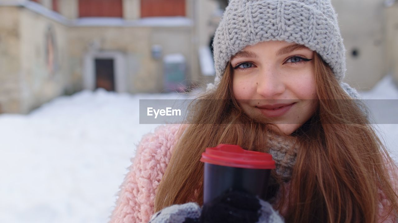 Portrait of young woman holding coffee cup while standing outdoors