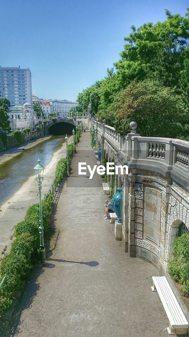 Sidewalk by canal in city against clear blue sky