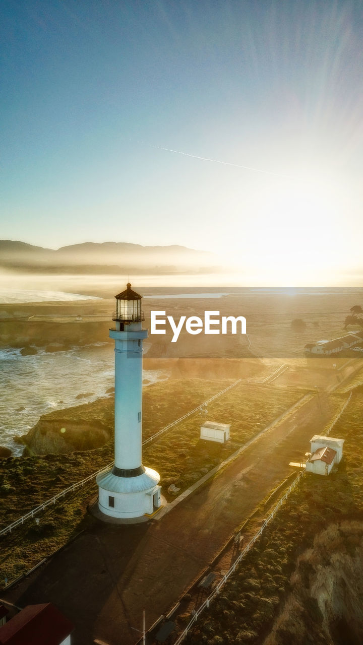 HIGH ANGLE VIEW OF LIGHTHOUSE AMIDST SEA AND BUILDINGS AGAINST SKY