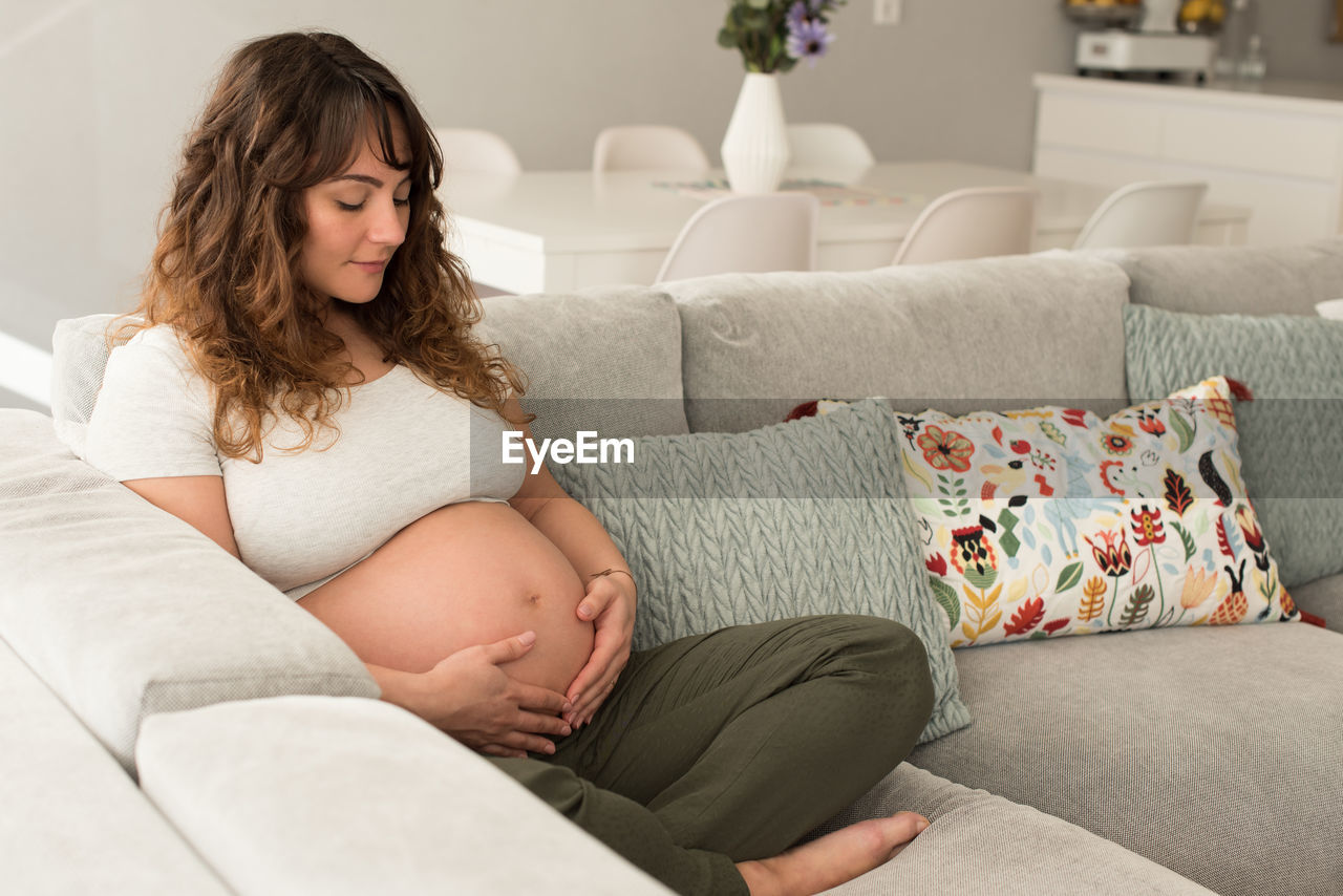 Full length of pregnant mid adult woman sitting on sofa at home