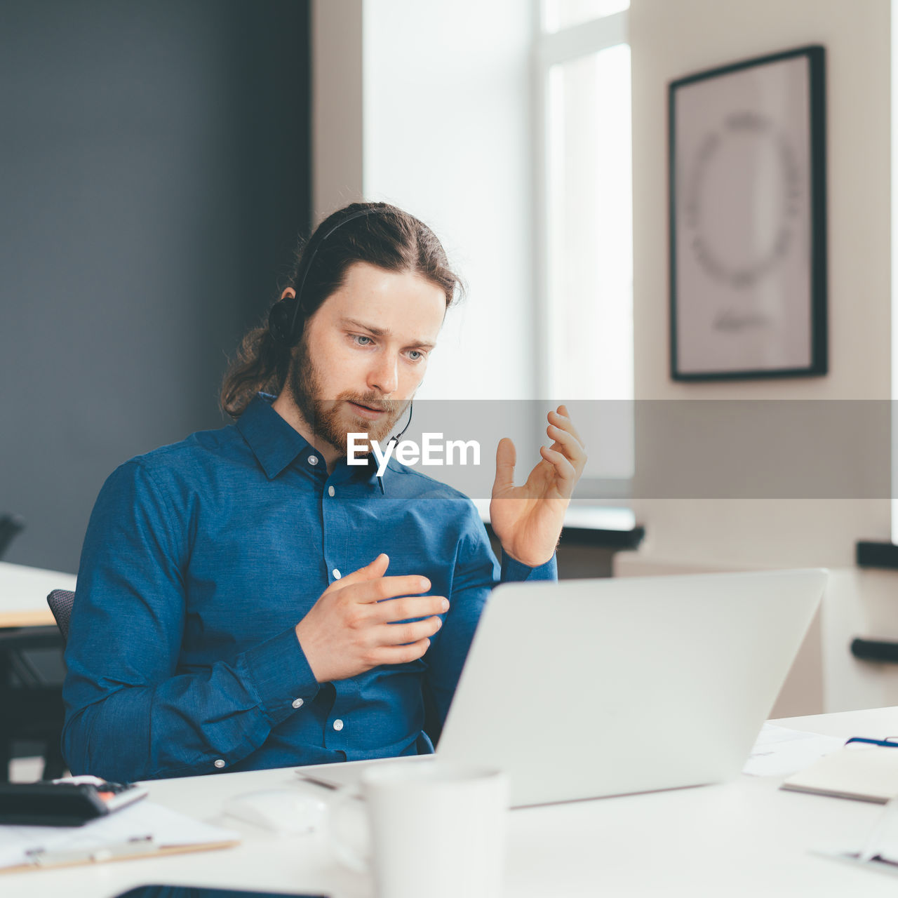 Concentrated young man operator in headset and casual wear talking with client on laptop in office