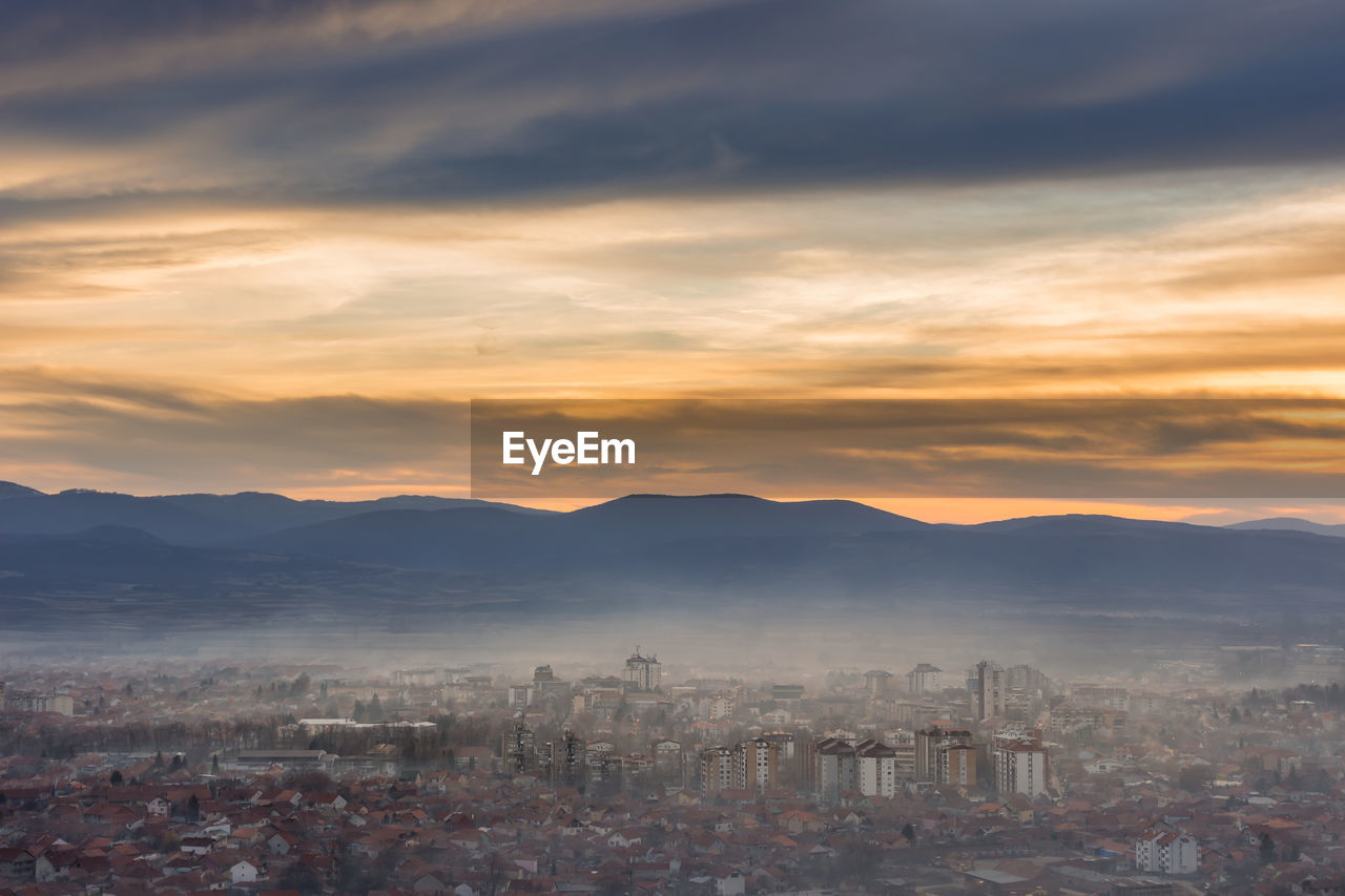 HIGH ANGLE VIEW OF TOWNSCAPE AND MOUNTAINS AGAINST SKY DURING SUNSET