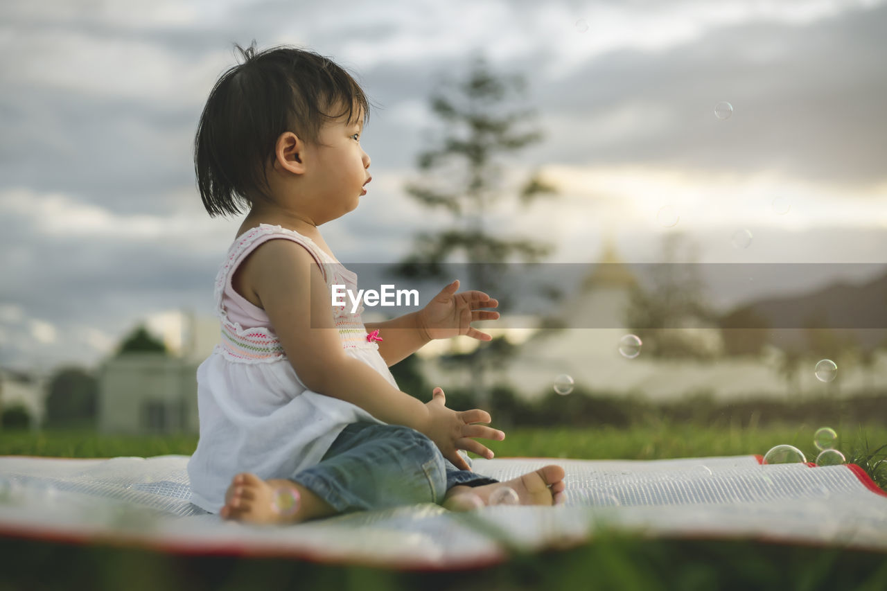 Side view of cute baby girl looking away while sitting on mat