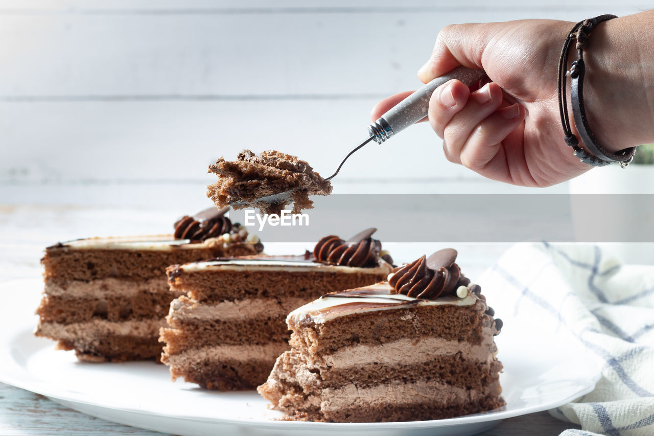 Hand holding a slice of delicious chocolate cake with fluffy cocoa sponge and marble effect icing.