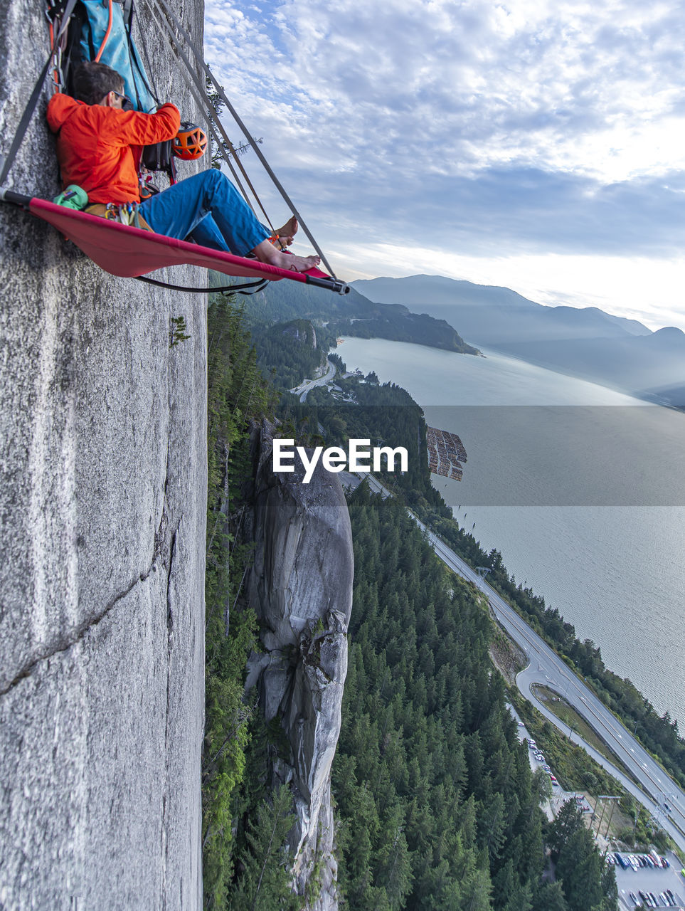 Side view of man sitting on portaledge organizing gear at sunset