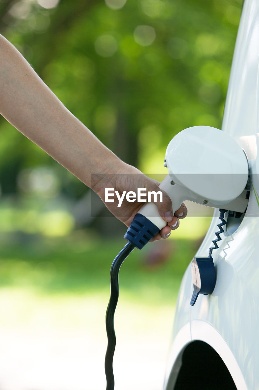 Cropped hand charging car at station