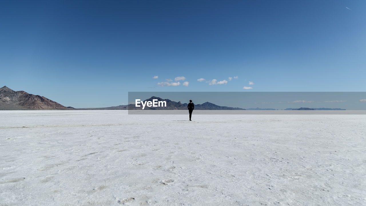 Rear view of person standing on salt flat against sky