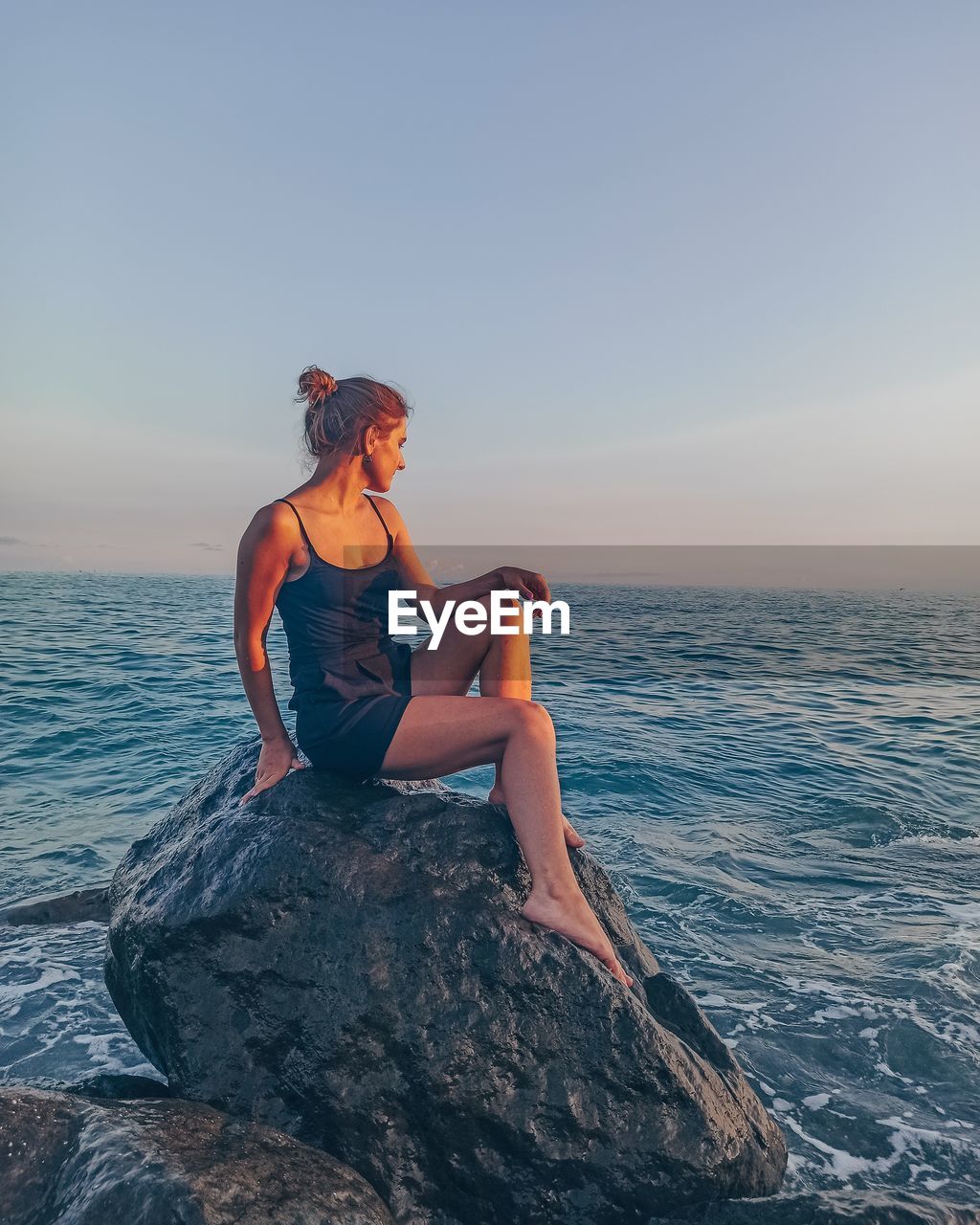 Woman sitting on rock by sea against sky