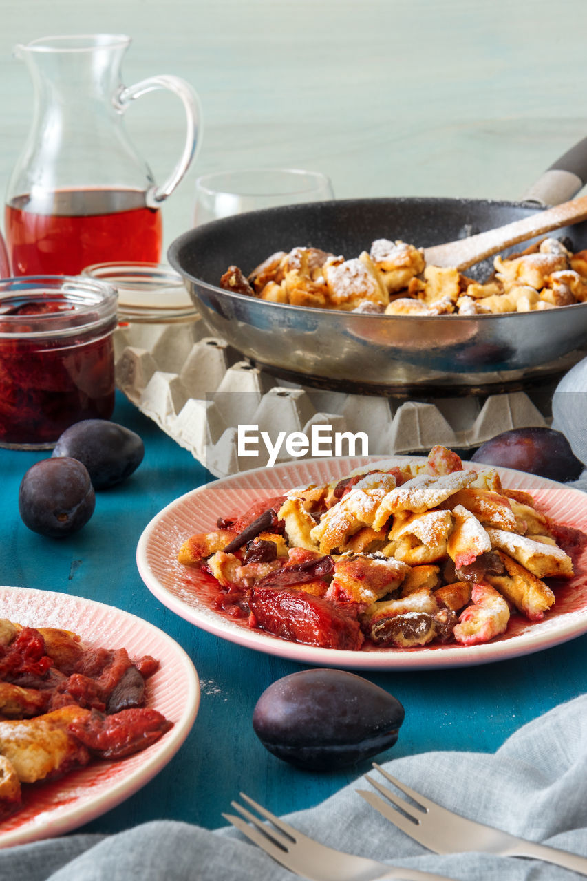 Low angle close-up kaiserschmarrn, austrian pancake dessert, with plums and raisins on white table.