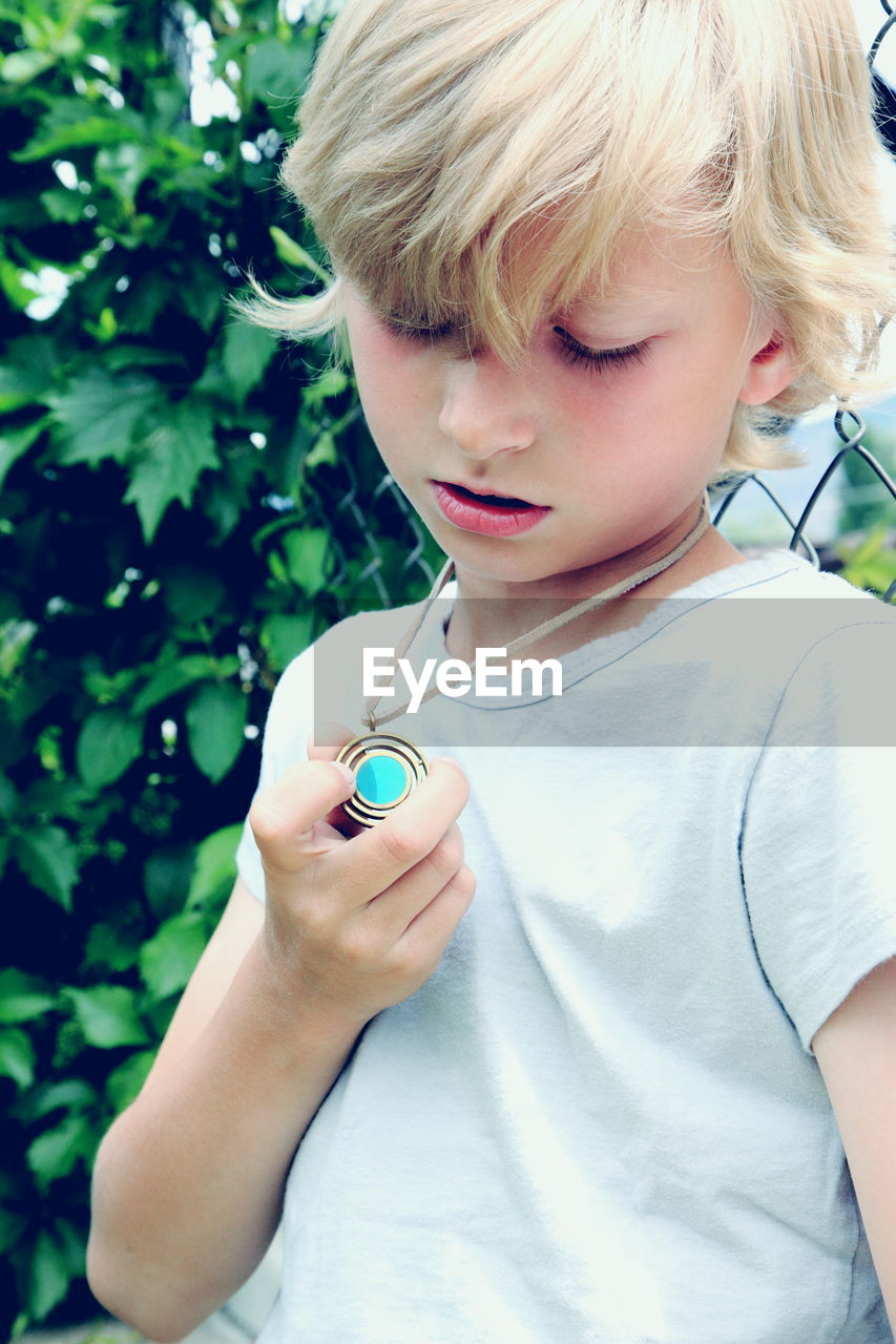 Close-up of boy looking at pendant necklace outdoors