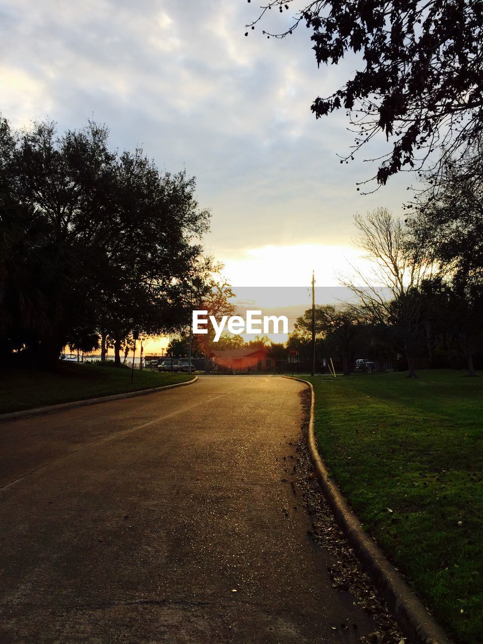 Road on field by trees against sky at sunset