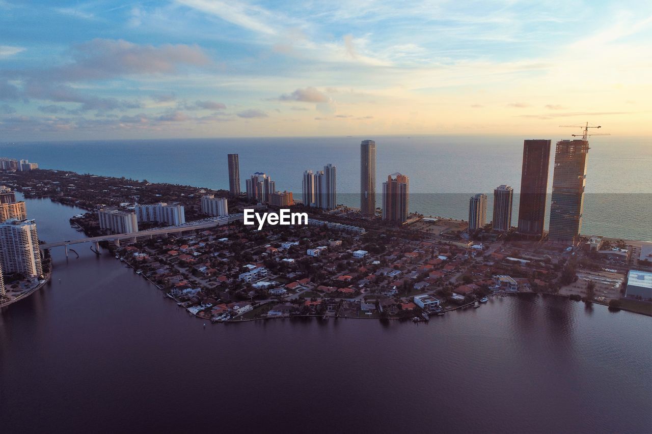 Aerial view of city by sea against sky during sunset