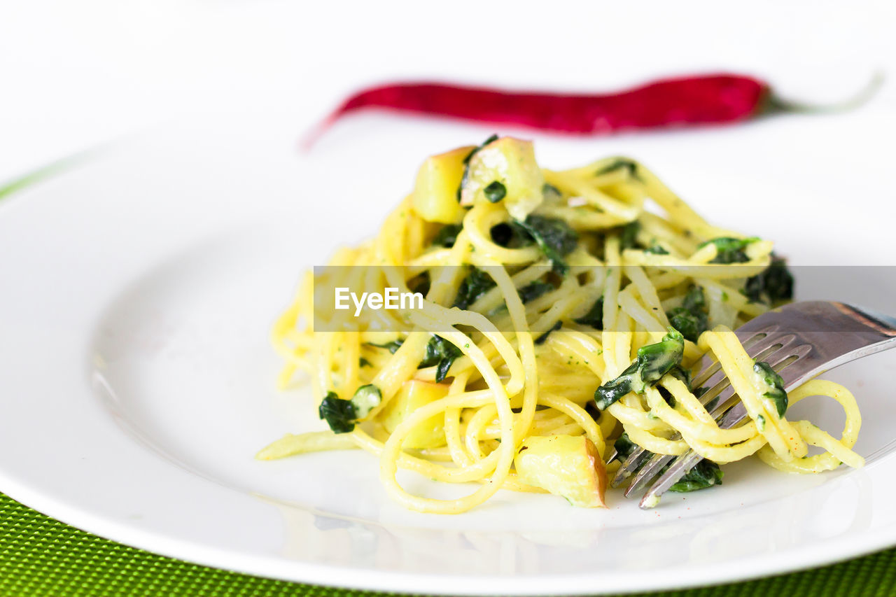 Close-up of fresh spaghetti with red chili pepper served in plate against white background