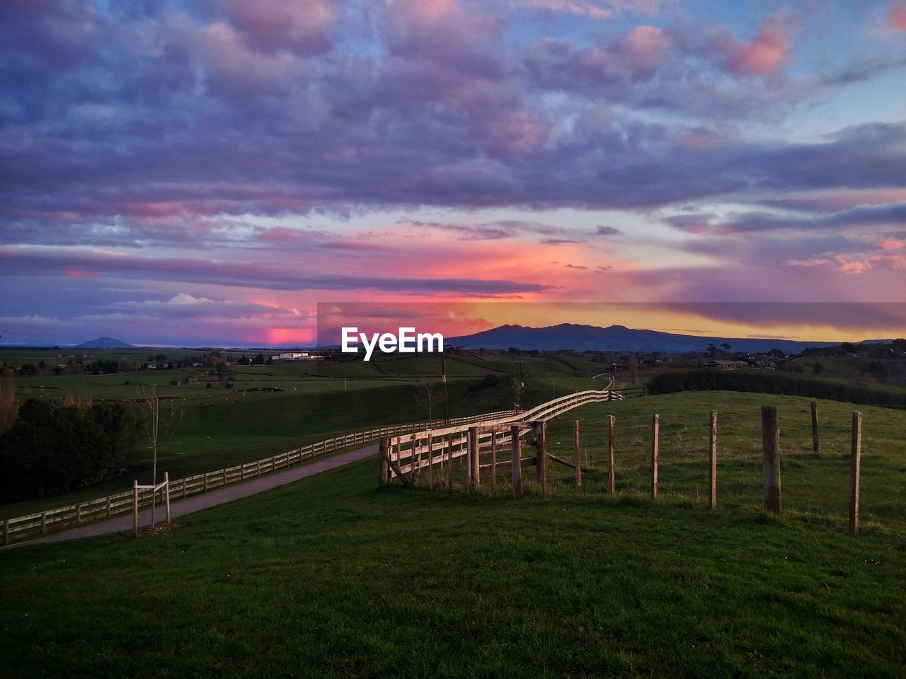 Scenic view of landscape against cloudy sky at sunset