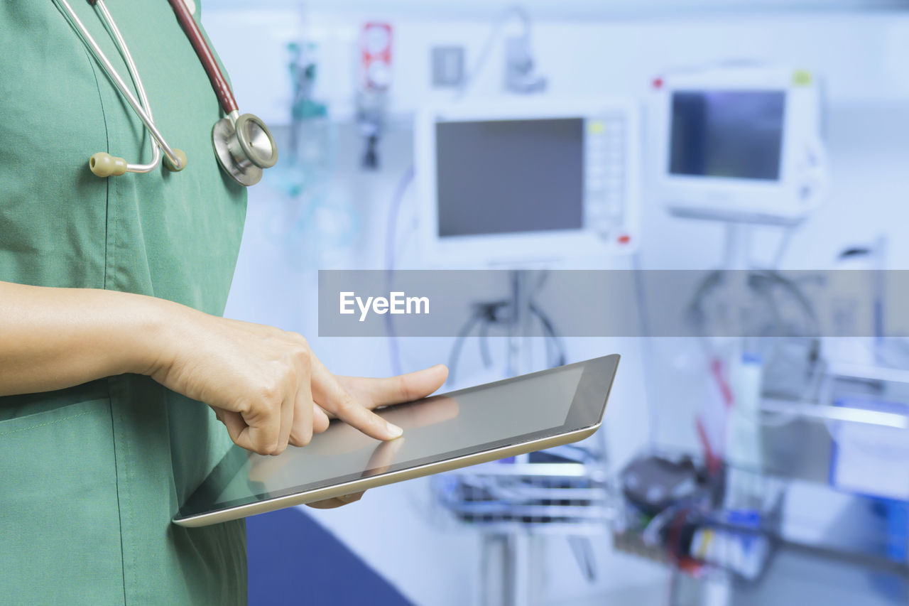 Midsection of nurse using digital tablet at hospital