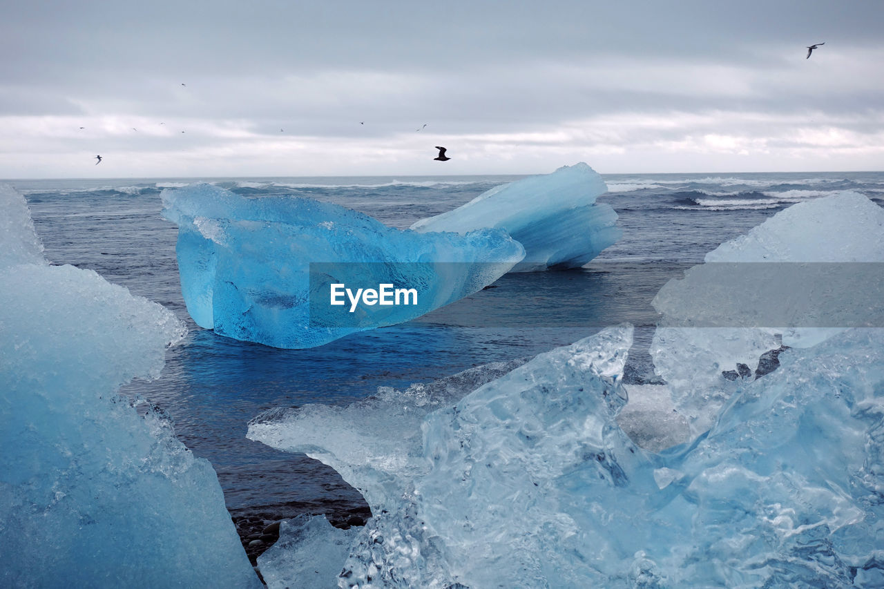 Ice on shore at beach against cloudy sky during winter