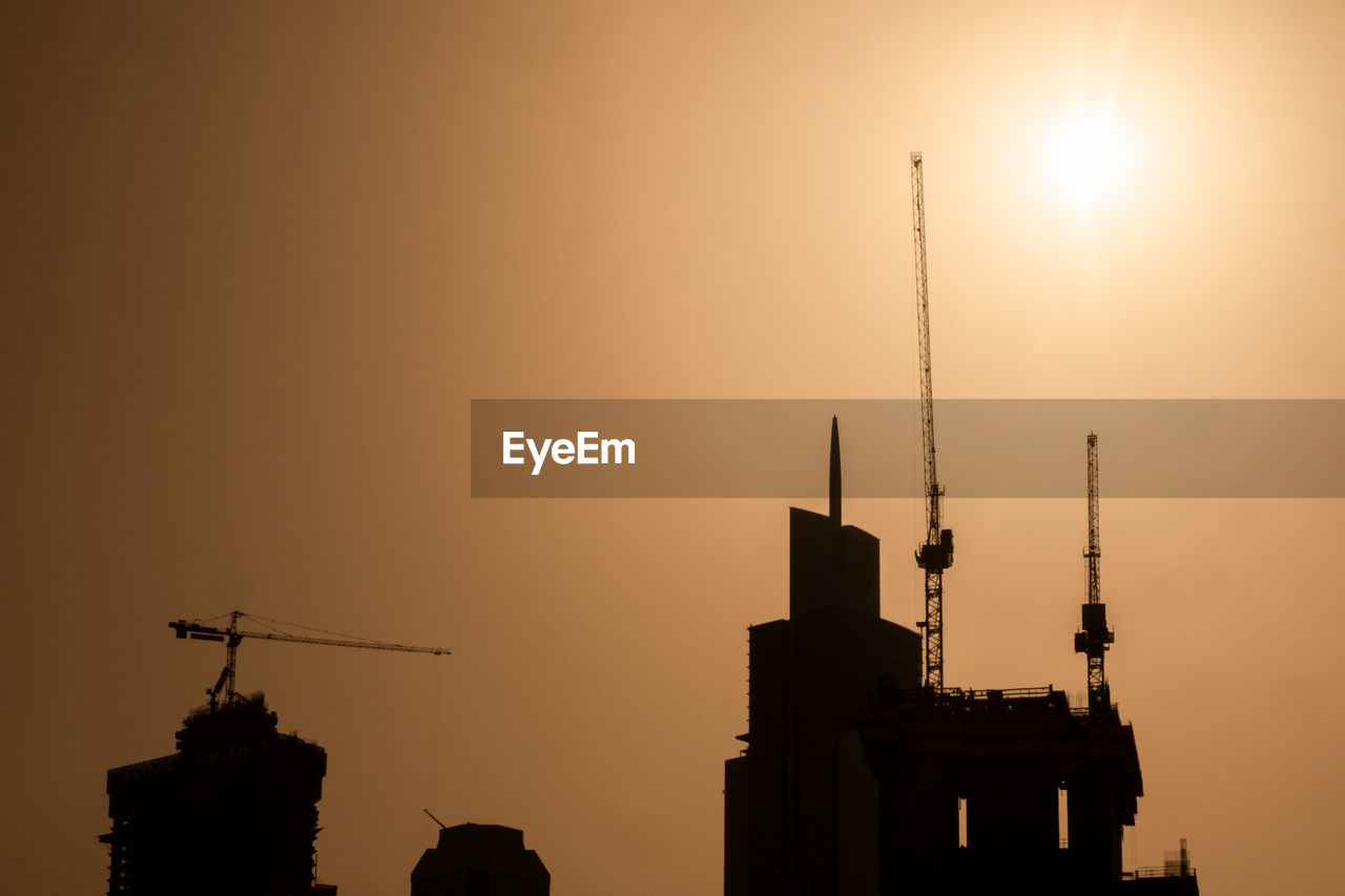 Low angle view of cranes at construction site during sunset