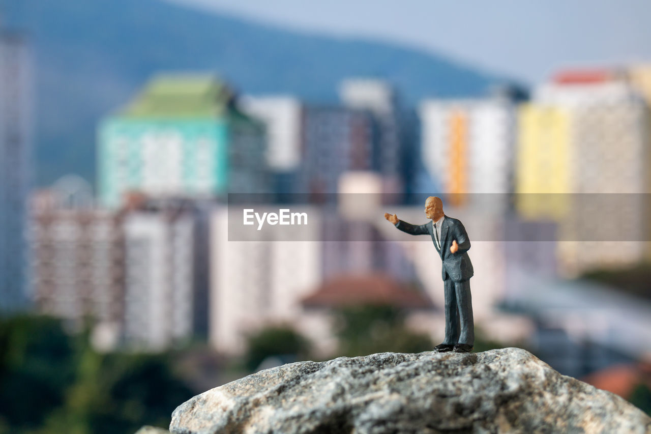 CLOSE-UP OF TOY ON ROCK AGAINST BUILDINGS