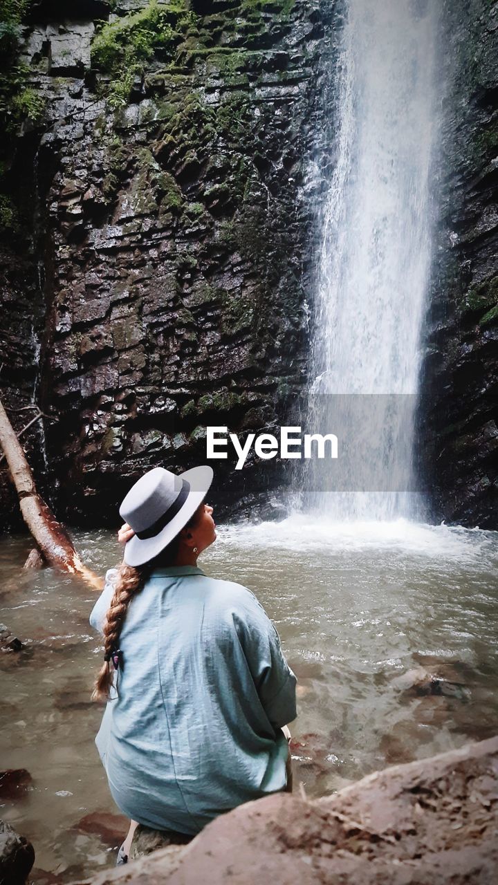 Rear view of woman standing in waterfall