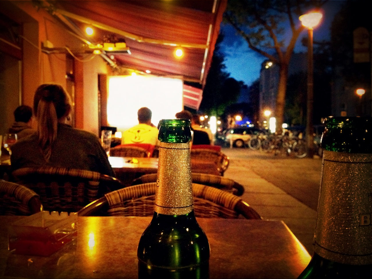 People at an outdoor restaurant with beer bottles in foreground