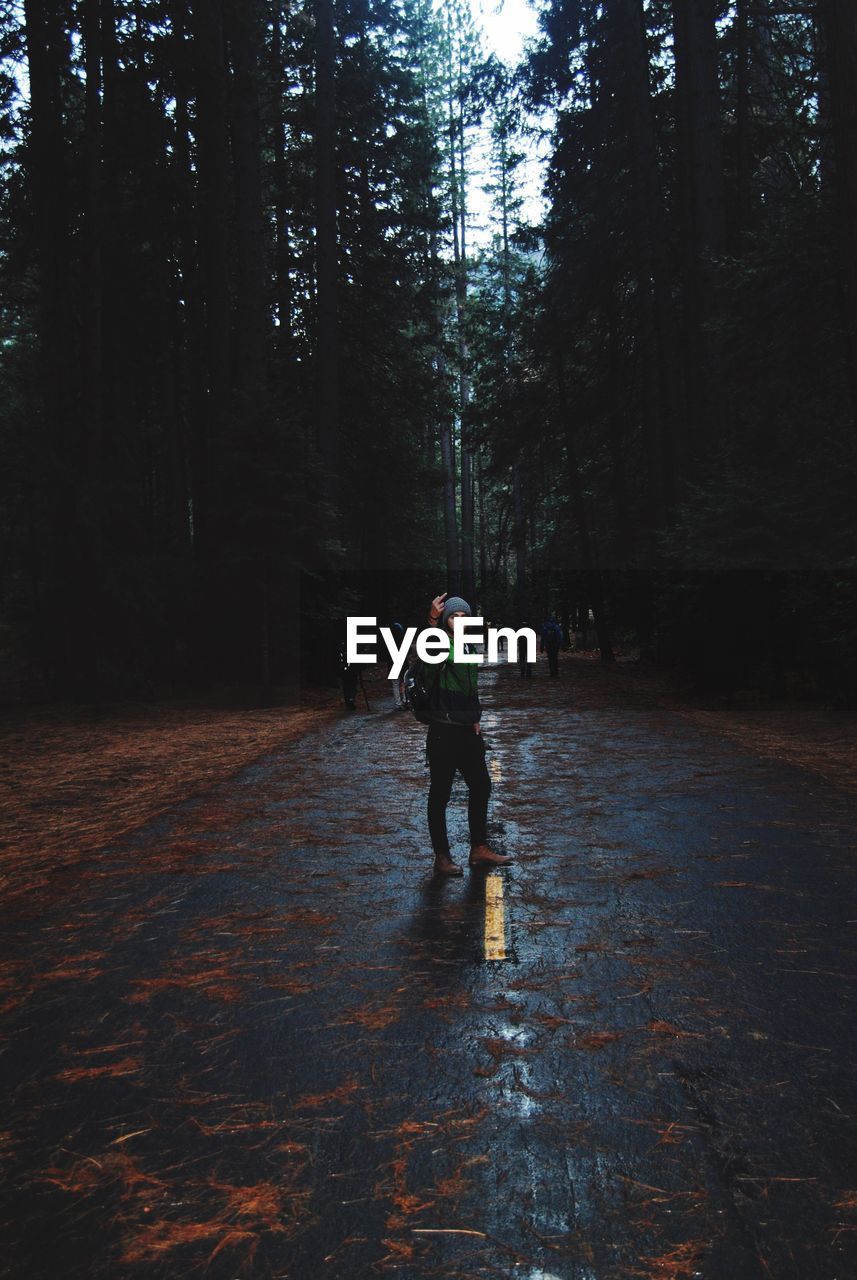 Full length of man showing middle finger while standing on road at forest