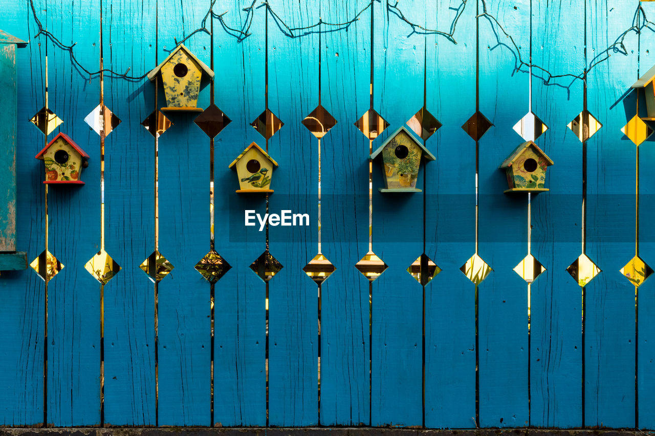 FULL FRAME SHOT OF BLUE HANGING ON METAL FENCE AGAINST WALL