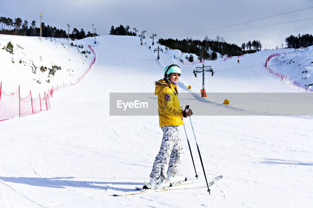  smiling young woman in yellow jacket ski helmet skiing on mountain slope, winter sports, alpine ski