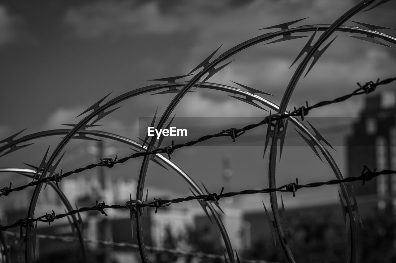 Low angle view of razor wire and barbed wire fence against sky