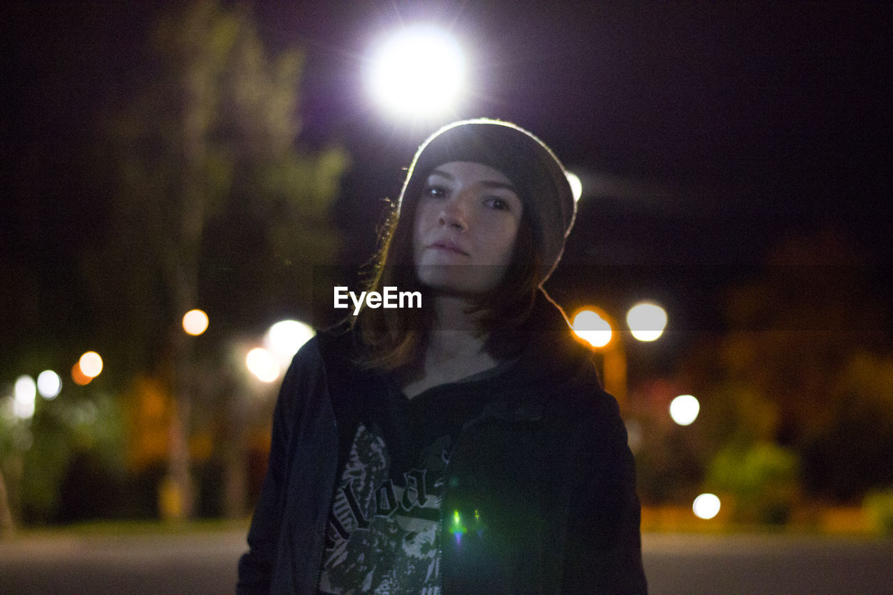 Portrait of young woman standing against at night