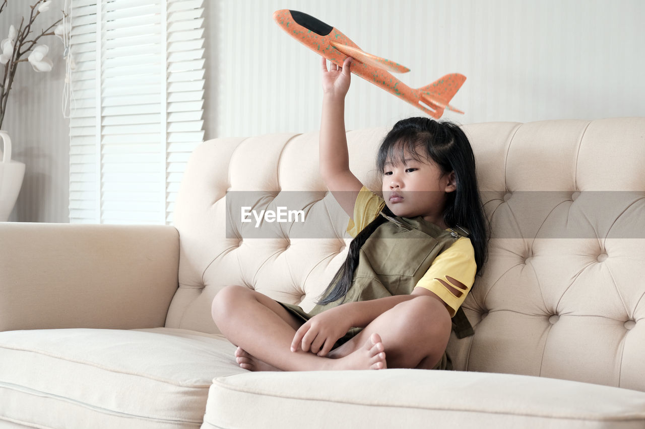 Asian kid sitting alone on the sofa inside the house on the plane with a feeling of not having fun