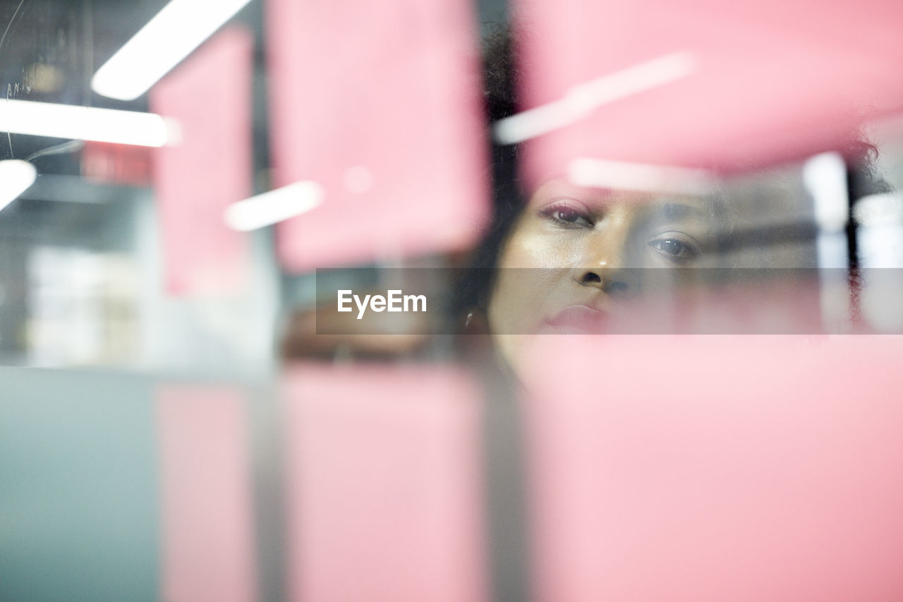 Businesswoman writing on adhesive notes seen through window in office
