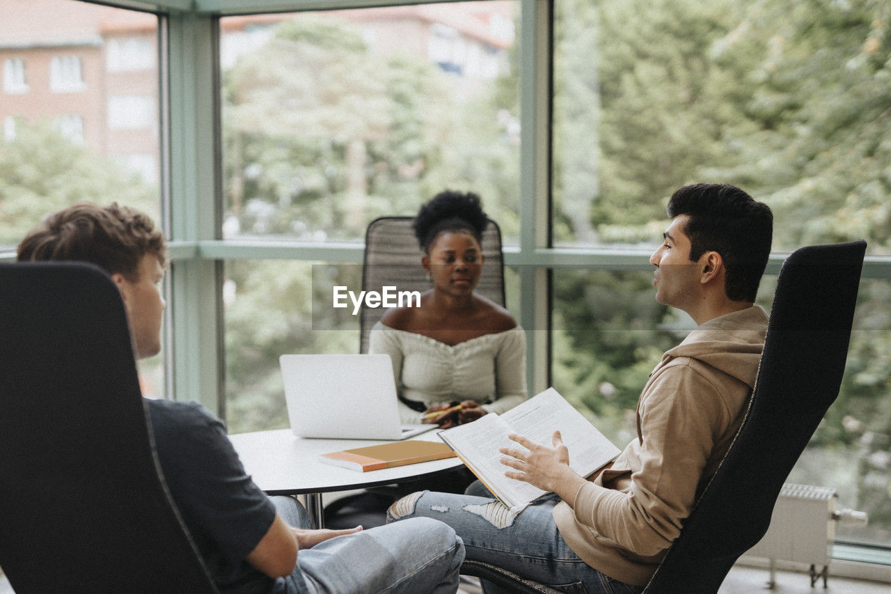 Multiracial students discussing while studying together in university