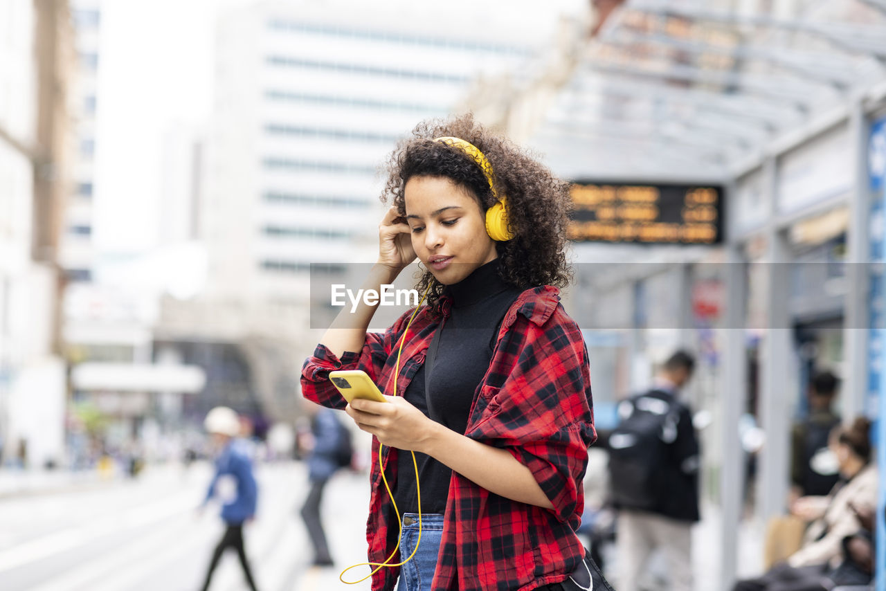 Young woman wearing headphones and using smart phone in city