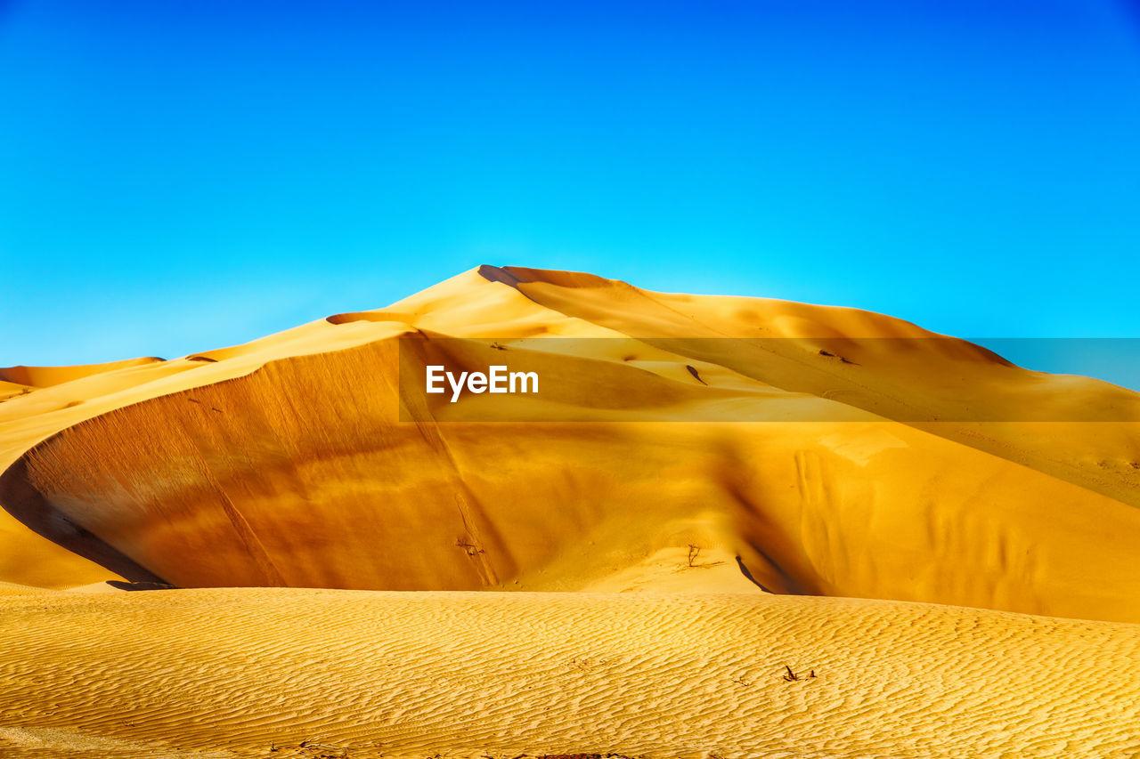 Sand dunes in desert against clear blue sky