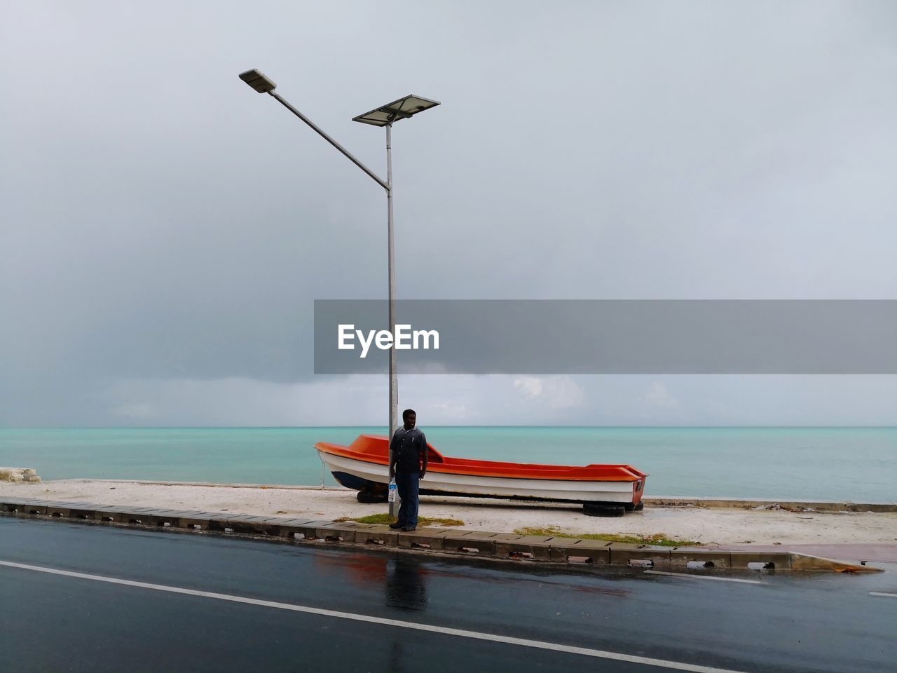 Full length of man standing by street light against sea and sky