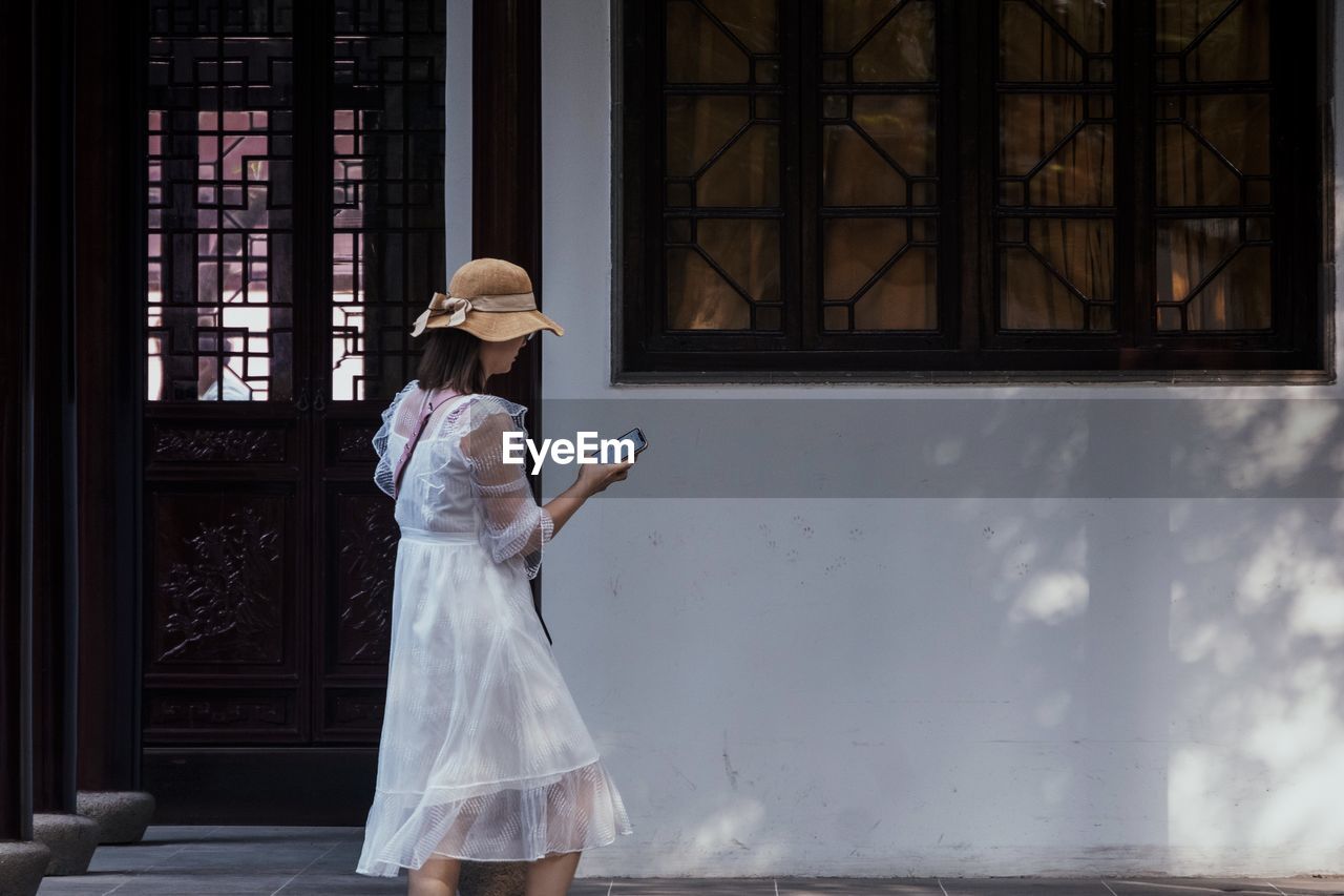 Young woman using smart phone standing by building