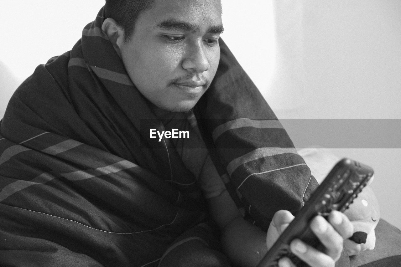 PORTRAIT OF YOUNG MAN SITTING ON TABLE AT HOME