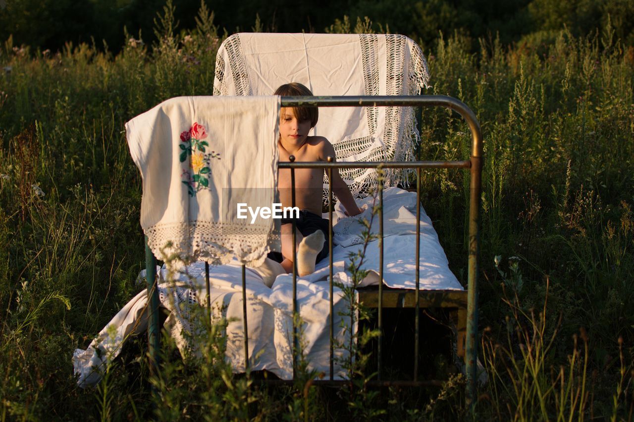 Full length of shirtless boy sitting on rusty bed at park