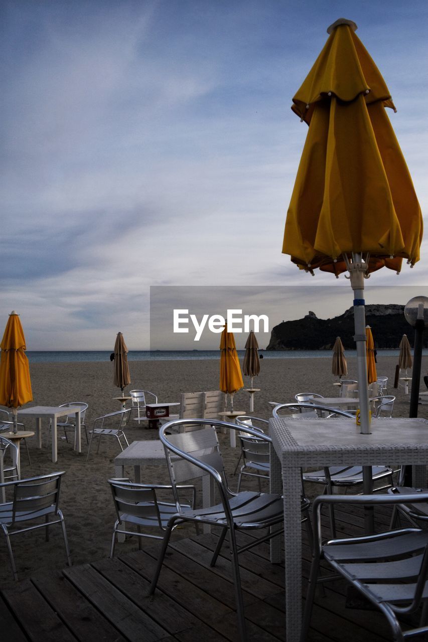 sky, sea, chair, water, beach, land, seat, nature, umbrella, parasol, vacation, table, holiday, trip, horizon, travel destinations, beauty in nature, horizon over water, tranquility, relaxation, summer, travel, sand, scenics - nature, cloud, sunset, tranquil scene, no people, absence, beach umbrella, outdoors, outdoor chair, sunshade, ocean, shade, dusk, idyllic, lounge chair, tourism, furniture