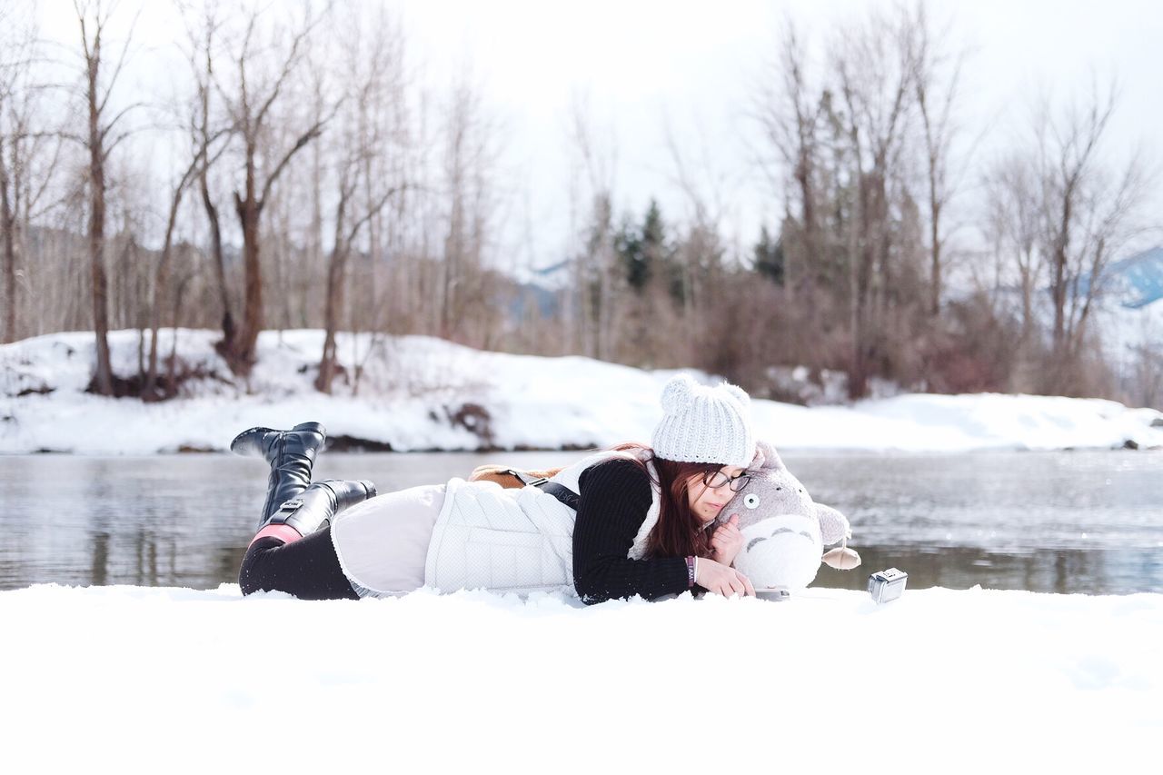 Full length of young woman with toy lying on snow by lake