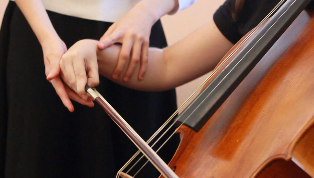 Midsection of musician teaching cello to woman