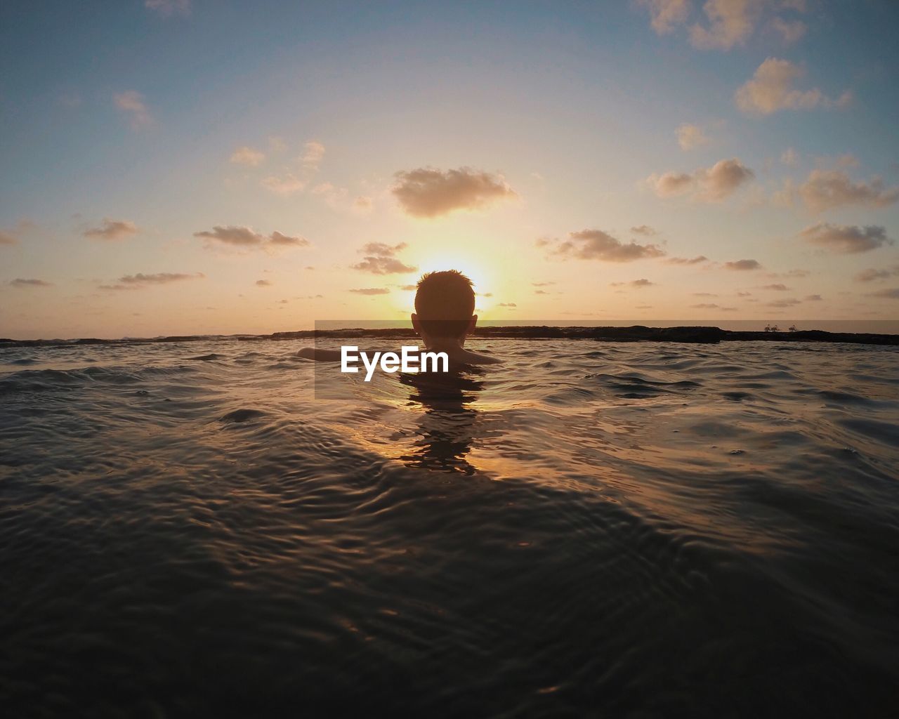 Rear view of man swimming in sea against sky during sunset
