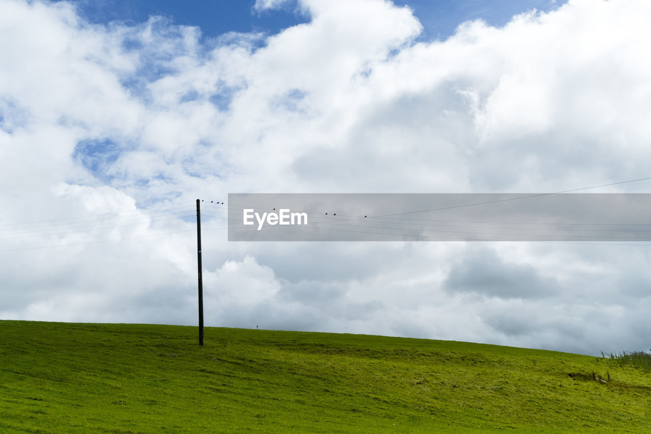 Electricity pylon on grassy field against cloudy sky