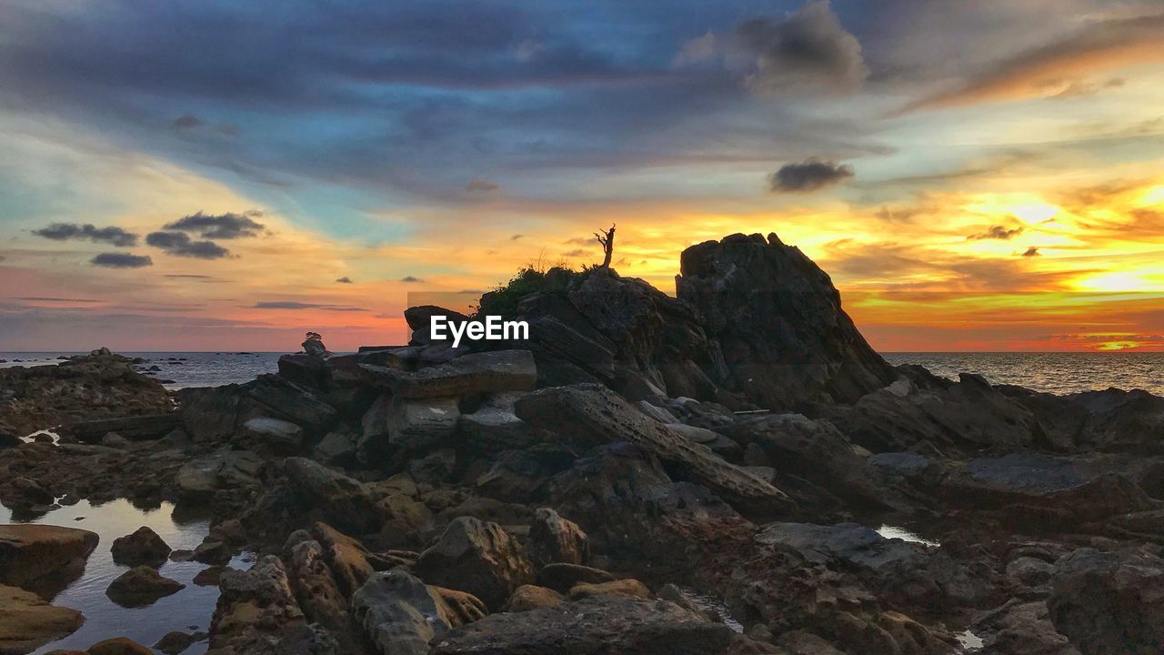 ROCK FORMATION ON SHORE AGAINST ORANGE SKY