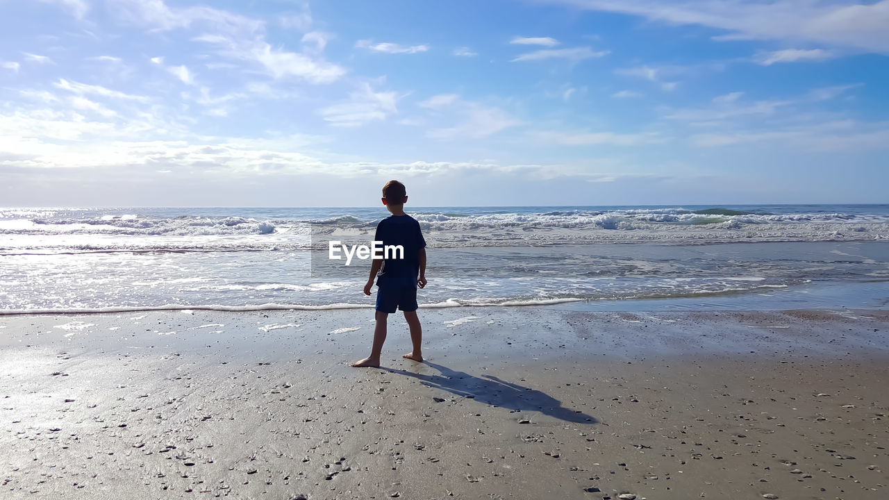 Rear view of boy standing against sea at beach